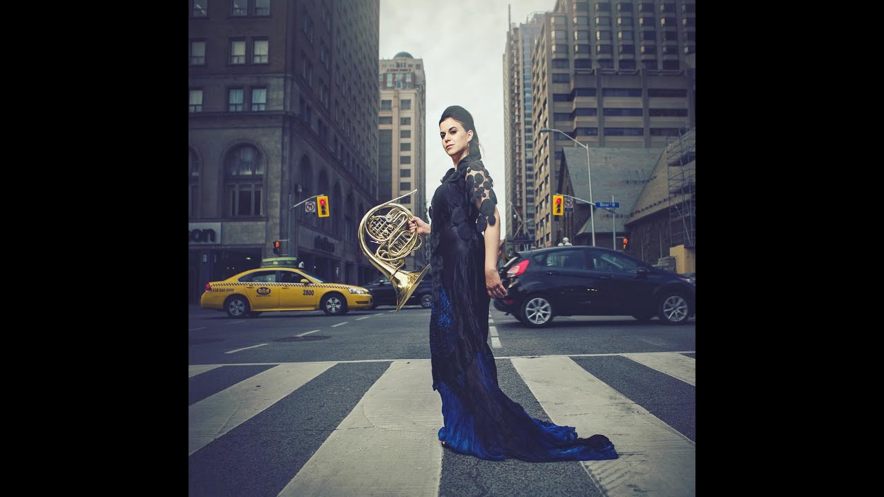 Woman holding a french horn standing in traffic