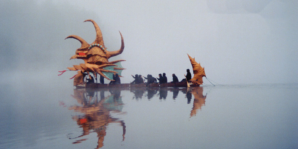 Large decorated canoe with 12 people on a misty lake